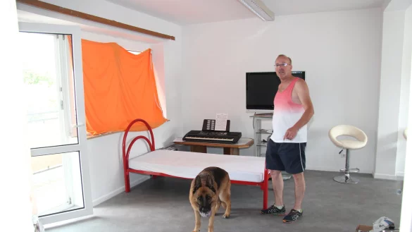 Franz Lozada (mit seinem Hund) hilft ehrenamtlich der ukrainischen Familie und zeigt das Wohnzimmer in der ansonsten ger&auml;umigen Dachgeschosswohnung. - &copy; Cordula Gr&ouml;ne(LZ)