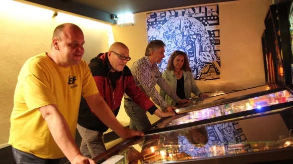 Nils Ponath (von links), Martin Langenau, Kim und Margit Danielmeier spielen an den Flippern in den Vereinsräumen. Das Bild im Hintergrund hat Langenaus Frau nach dem Vorbild eines Flippers gemalt. - © Nadine Uphoff