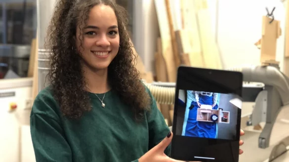 Rita Bierl hat in ihrem Studium in Detmold ein besonderes Möbelstück entworfen und in der Holzwerkstatt der TH OWL (im Hintergrund) gebaut. Der inklusive Nachttisch ist auf dem Tablet zu sehen. - © Till Brand