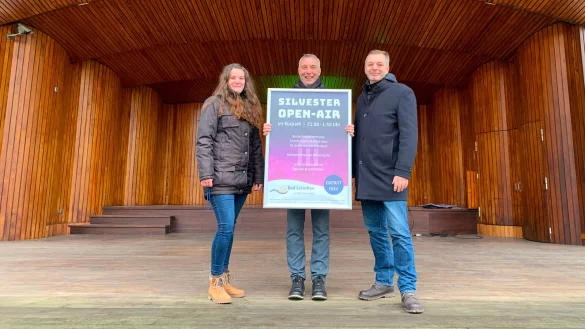 Leonie Immel (von links, Eventmanagement), B&uuml;rgermeister Dirk Tolkemitt und Oliver Siekmann (Stadtmarketing) pr&auml;sentieren das Plakat zum Silvester Open-Air in der Konzertmuschel im Kurpark. - &copy; Stadt Bad Salzuflen