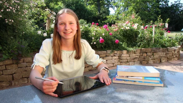 Charlotte Umfermann mit Schulbüchern und Tablet im Garten ihres Elternhauses. - © Jana Beckmann
