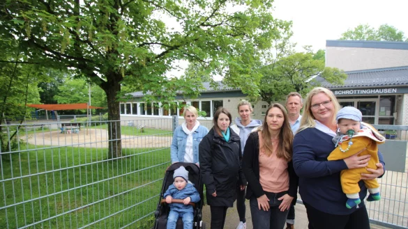 Julia Althoff mit Luca (2, v.l.), Jessica Rabe, Rebecca Gruhn, Janine Barth, Benjamin Borm und Janina Dierkes mit Henry (4) stehen vor dem Zaun der Kita. Im Hintergrund ist der Bereich f&uuml;r Kinder unter drei Jahren zu sehen. - &copy; Sylvia Tetmeyer