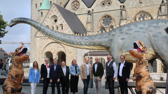 Die Organisatoren von "Dinoborn" posieren vor dem Paderborner Dom mit dem an einem Baum naschenden Diplodocus. - © Maria Kalemi