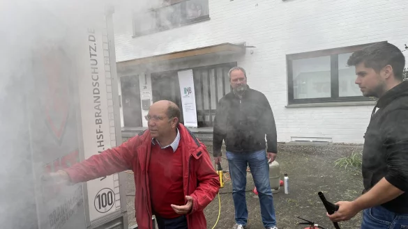Die Brandschutzexperten Klaus Meding (von links) und Christian von Borck demonstrieren LZ-Volontär Philipp Kersten den Brandsimulationswagen. - © Nico Düllmann