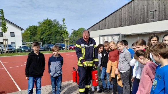Bei der Station der Freiwilligen Feuerwehr erkl&auml;rt ein Feuerwehrmann den Kindern, wie sie ein Feuer l&ouml;schen k&ouml;nnen. - &copy; Franka Ronkartz (LZ)