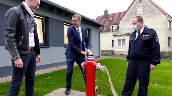 Mit Inbetriebnahme des Hydranten gilt das Feuerwehrger&auml;tehaus offiziell als &uuml;bergeben. Wilhelm Luft vom Architekturb&uuml;ro Schmidt (links), B&uuml;rgermeister J&ouml;rg Bierwirth und Marc Tegeler, Einheitsf&uuml;hrer W&ouml;bbel, freuen sich. - &copy; Rudi Rudolf