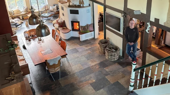 Martin Dauer steht in der Deele im Eingang zur K&uuml;che. Der Raum mit seinem gro&szlig;en Esstisch und dem Kamin ist Mittelpunkt des Hauses. Die Matratze vorne rechts dient als Schlafplatz f&uuml;r die Hunde. - &copy; Sven Kienscherf