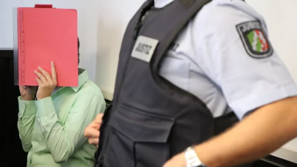 Die Angeklagte verdeckt beim Prozessauftakt ihr Gesicht mit einem roten Aktendeckel. - © Holger Kosbab