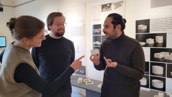 Lena Kopsieker und Lando Schumpich (Mitte) h&ouml;ren von Mohamed Khaled, wie er das Programm f&uuml;r den 3D-Drucker ver&auml;ndert hat, um die feinen wellenf&ouml;rmigen Oberfl&auml;chenstrukturen herauszuarbeiten. - &copy; Astrid Sewing
