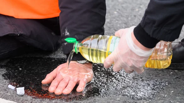 Polizisten l&ouml;sen die festgeklebten H&auml;nde der Klima-Aktivisten mit Speise&ouml;l von der Stra&szlig;e. - &copy; Julian Stratenschulte / dpa