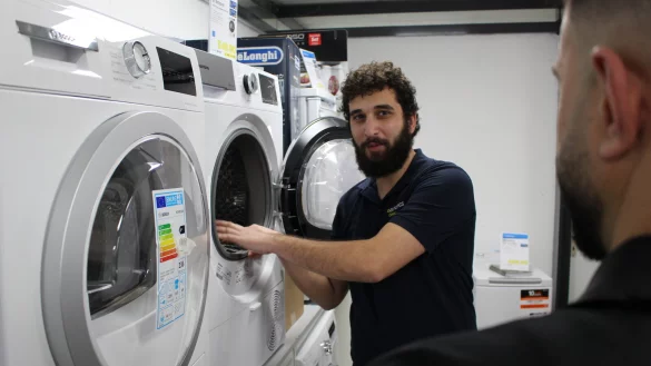 Ahmet Cekic zeigt in seinem Elektronik-Laden einem Kunden einen Wäschetrockner und erklärt die Funktionen. - © Pauline Maus