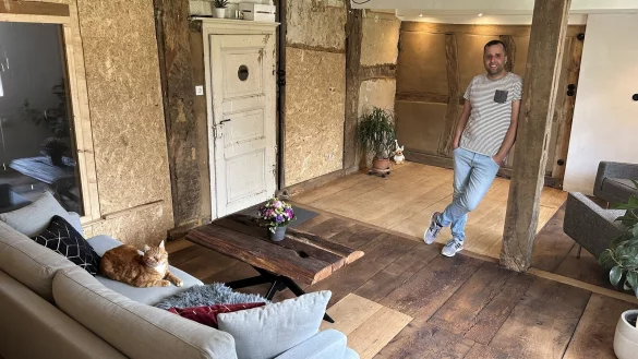 Murat Erbach mit Kater "Floki" im fertig sanierten Wohnzimmer des denkmalgeschützten Haupthauses seines Hofes - später, sobald die Diele fertig ist, werden die Gefache, die jetzt noch mit OSB-Platten verkleidet sind, geöffnet. - © Alexandra Schaller