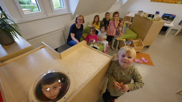 Ensar schaut durchs Guckloch, Paul steht rechts neben der Spielh&ouml;hle. Im Hintergrund sitzen Erzieherin Heike Sch&auml;pe, Lina, Sophia, Elif, Isabella, Stella und Alia. - &copy; Jost Wolf