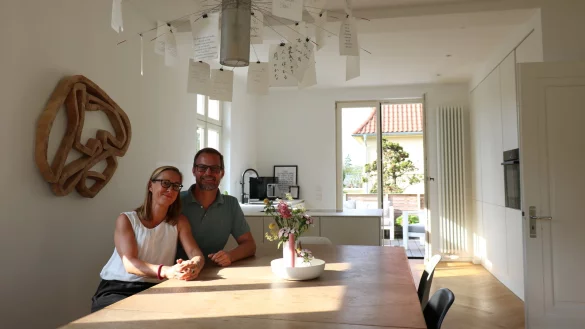 Sandra und Oliver St&ouml;vesand sitzen am wuchtigen Holztisch im gro&szlig;z&uuml;gigen Wohn- und Essbereich ihrer Villa am Fliederweg - im Hintergrund die moderne K&uuml;che und der neu geschaffene Zugang zum Garten. - &copy; Alexandra Schaller