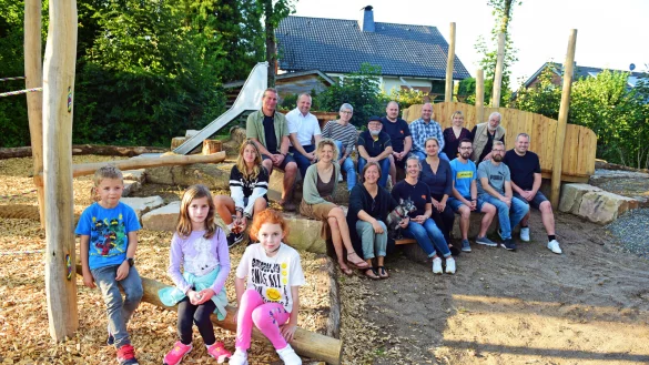 Henry, Malina und Marlene (von links) freuen sich &uuml;ber den neuen Spielplatz, den die Helfer im Hintergrund f&uuml;r sie gebaut und gestaltet haben. - &copy; Nicole Ellerbrake