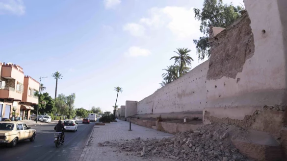 Menschen fahren nach dem Erdbeben an einer besch&auml;digten Mauer der historischen Medina vorbei. Urlaub in Marrakesch soll bereits wieder m&ouml;glich sein. - &copy; Mosa'ab Elshamy/dpa