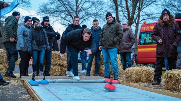 Zielsicherer Wurf: Florian Duda von Team der &bdquo;hauptamtlichen Kr&auml;fte&ldquo; setzt an und feuert den Eisstock &uuml;ber die Plane. Im Hintergrund dr&uuml;cken Jannik Wiesekopsieker, Timo Wessel und Stefan Johannsmeyer (von links) die Daumen. Das Team vom &bdquo;L&ouml;schtrupp Holzhausen&ldquo; links zittert mit. - &copy; FreitagTV/Stock