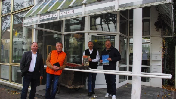 Kurdirektor Thorsten Brand (rechts) h&auml;lt ein altes Veranstaltungsjournal in der Hand, B&uuml;rgermeister Heinz-Dieter Kr&uuml;ger die Brosch&uuml;re zum 100-j&auml;hrigen Bestehen des Staatsbades. Zusammen mit Michael Lohmeier vom St&auml;dtischen Bauamt und Arne Brandt vom Landesverband Lippe (links) stehen sie vor dem Eingang der einstigen Kurverwaltung, die eine alte h&ouml;lzerne Moorwanne ziert. - &copy; Dieter Asbrock