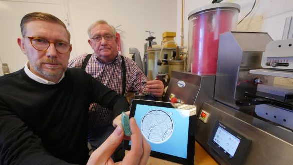 Die Goldschmiede Achim und Wolfgang Sch&auml;ffer (von links) zeigen einen Teil des Herstellungsprozesses vom 3D-Modell zum fertigen Schmuck. Auf dem Tablet ist das per Computer entworfene Modell zu sehen, aus dem eine Pforzheimer Firma dann ein t&uuml;rkisfarbenes Wachs-Kunststoff-Positiv druckt, wie das, was Achim Sch&auml;ffer in der Hand h&auml;lt. Damit wird eine Silikonform erstellt, wie sie rechts als Block in der Maschine liegt. Diese wird mit pinkfarbenen Wachs ausgegossen, so dass ein Modell entsteht, wie es Wolfgang Sch&auml;ffer in der Hand h&auml;lt. Damit wird schlie&szlig;lich eine Gipsform erstellt, die dann mit Gold oder Silber f&uuml;r den Schmuck ausgegossen wird. - &copy; Jost Wolf