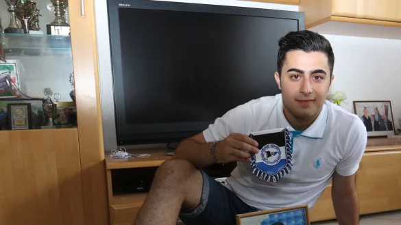 Ein Foto vor dem Troph&auml;enschrank: Nujin Hassan pr&auml;sentiert stolz das Bild, das ihn im Arminia-Trikot zeigt. Hinter ihm sind etliche Pokale zu sehen. - &copy; Oliver K&ouml;nig