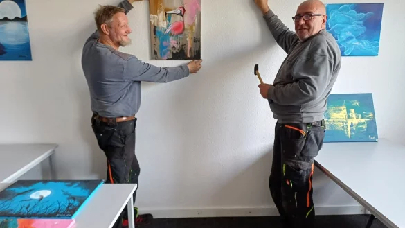 Die Mitarbeiter des Vereins "Arbeit Werkstatt Bildung" Hartmut Strunk (links) und Torsten Filges h&auml;ngen die Bilder auf. - &copy; awb