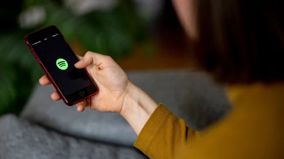 Eine Frau &ouml;ffnet die Spotify-App auf ihrem Handy - &copy; Foto: Fabian Sommer/dpa/dpa-tmn