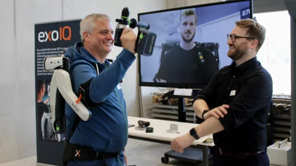 Markus Römisch probiert das Exoskelett aus, Robert Lux von ExoIQ gibt Anleitung. - © Nina Schroeder