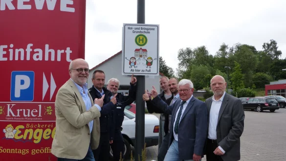Am neuen Schild: (von links) Schulleiter Michael Gerd Schnittger, Michael Behler und Carlo Bahms von der Polizei Detmold, &bdquo;Michels Multistore"-Inhaber Michel Veensma, Rewe-Leiter Jan Christoph Kiwitt, Karsten Seefeldt von der Kreisverkehrswacht Lippe sowie Ortsb&uuml;rgermeister Rainer Friedrich werben f&uuml;r die Nutzung der Elternhaltestelle am Rewe-Markt. - &copy; privat