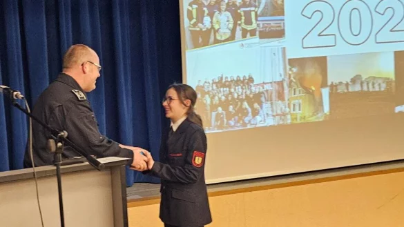 Der Leiter der Feuerwehr Lage, Benjamin Brinkmeyer, gratuliert Amelia Heel, die am Tag der Jahreshauptversammlung ihren 15. Geburtstag feierte und es sich nicht nehmen ließ, mit dem Spielmannszug in der Aula am Werreanger aufzutreten. - © Astrid Sewing