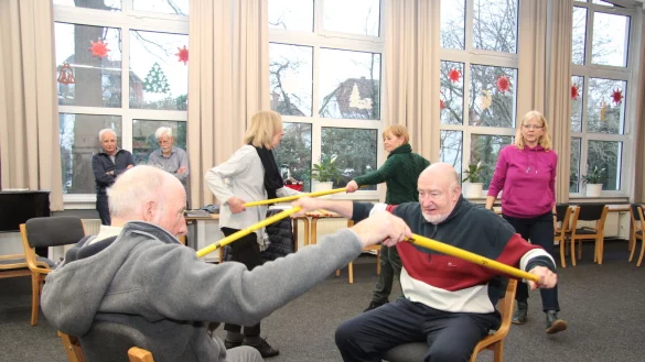 Beim Rehasport schauen (hinten, von links) G&uuml;nter Notbohm und Uwe K&ouml;llermeyer zu, w&auml;hrend Ghislaine Nauwelaerts, Karin Rose, Dieter Strate und Sieghard Schneider, angeleitet von Krankengymnastin Annegret Pivit, &Uuml;bungen mit Stangen und B&auml;llen machen. - &copy; Cordula Gr&ouml;ne