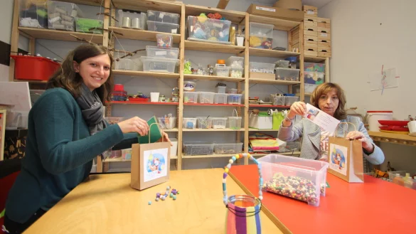 Erzieherin Viktoria Bergen (links) und Einrichtungsleiterin Sabine Neumann packen T&uuml;ten mit Bastel-Sets f&uuml;r den guten Zweck. Im Vordergrund steht ein fertig gestaltetes Lichtglas. - &copy; Jens Rademacher