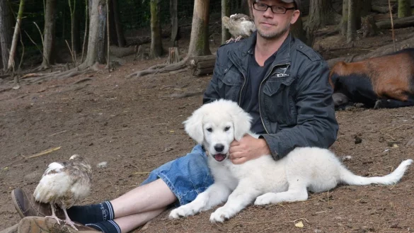 Henry Frenzel sitzt mit seinem Herdenschutzhund-Welpen &bdquo;Capone" auf der Koppel zwischen Ziegen und Federvieh. Aus Sorge, ein junger Hund werde dort allein gelassen, hatten vermeintliche Tiersch&uuml;tzer ihn einfach mitgenommen.&nbsp; - &copy; Tanja Watermann