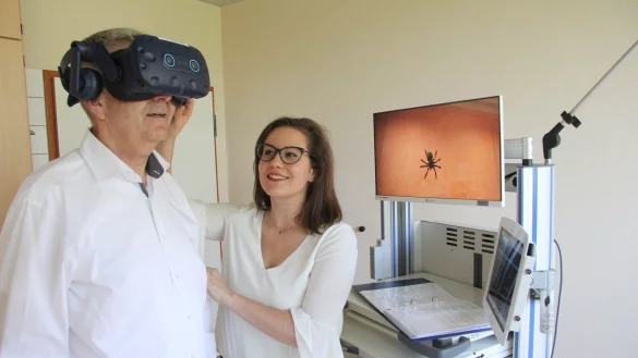 Psychologin Nicole Dukart passt das Headset der VR-Brille an, die Udo Schneider, Leiter des medizinischen Zentrums f&uuml;r seelische Gesundheit, aufgesetzt hat, um in eine virtuelle Welt mit Spinnen eintauchen zu k&ouml;nnen. - &copy; Carolin Nieder-Entgelmeier