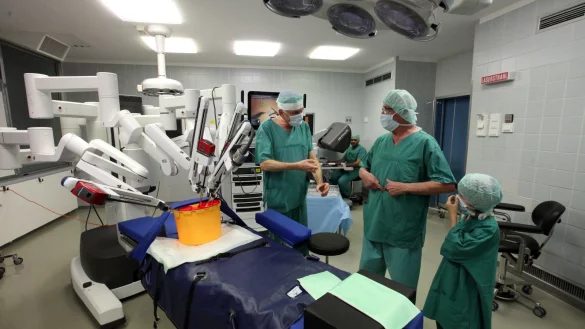 Pressetermin im OP-Saal: (von links) Chefarzt Dr. Alfons Gunnemann erklärt seinem Patienten Joachim Schlingmann, der mit Enkel Leonard gekommen ist, die Funktionsweise des Roboters. Im Hintergrund sitzt Oberarzt Ihab Abutabanjeh am Bildschirm der Maschine. - © Bernhard Preuß