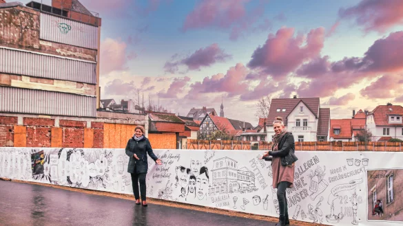 Dörte Pieper, Fachbereichsleiterin Kultur, Tourismus, Marketing und Bildungseinrichtungen bei der Stadt Detmold (links) und die Illustratorin und Designerin Nicole Sprekelmann vor dem verschönerten Bauzaun. - © Stadt Detmold