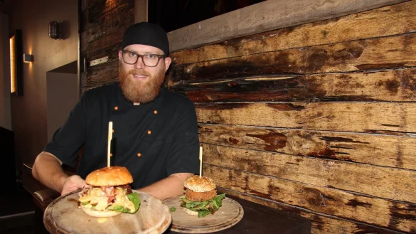 Sebastian Schraets präsentiert zwei Kreationen: Der eine Burger besteht aus einem vegetarischen Süßkartoffel-Walnuss-Bratling, getrockneten Tomaten und Büffelmozzarella, der andere aus Rindfleischpatty, Speck, Honig und Käsesauce. - © Kirsten Fuhrmann