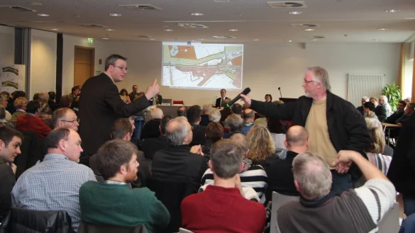 Alle H&auml;nde voll zu tun: Dr. Nicolas Rin&ouml;sl von der Bezirksregierung Detmold (links) hat den Er&ouml;rterungstermin im Tagungssaal des &bdquo;Best Western"-Hotels am Ostertor souver&auml;n geleitet und moderiert. Bernd Beermann, Anwohner des Riedwegs, reicht ihm nach einem Wortbeitrag das Mikrofon zur&uuml;ck. - &copy; Stefan Backe