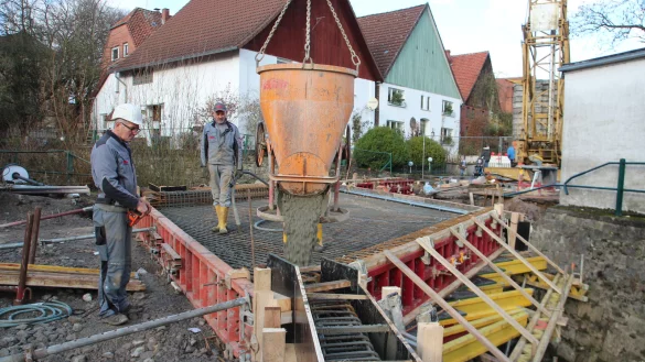 Mit Augenma&szlig;: Polier Jean Pierre Schiepers (links) l&auml;sst per Fernsteuerung den an einem Kran h&auml;ngenden K&uuml;bel &uuml;ber die Br&uuml;cke schweben, wo die Oberfl&auml;che betoniert wird. Mitarbeiter Gnardy Heide verteilt den Baustoff mit einem Betonr&uuml;ttler. - &copy; Patrick Bockwinkel