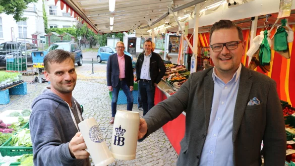 Maximilian Janski, Vorsitzender des Sch&ouml;tmaraner B&uuml;rgervereins, st&ouml;&szlig;t mit Andreas Pla&szlig;, Vorsitzender des Wochenmarktvereins, an dessen Gem&uuml;sestand an. Im Hintergrund Andr&eacute; Schr&ouml;der, stellvertretender Vorsitzender des B&uuml;rgervereins (links) und Oliver Siekmann vom Stadtmarketing. - &copy; Alexandra Schaller