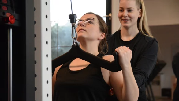 Beim Latzug wird vor allem der obere Rücken trainiert. Benita (hinten) motiviert mich, während ich die Stange nach unten ziehe. - © Sven Hauhart