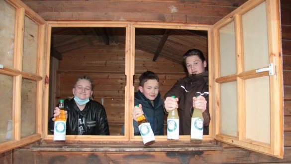 Normalerweise verkauft der Erg&auml;nzungskurs seinen Saft aus der Safth&uuml;tte heraus. Die ist momentan allerdings im Winterschlaf. Trotzdem pr&auml;sentieren Malo, Malte und Mathis (von links) stolz ihren Apfelsaft durch das Verkaufsfenster. - &copy; Karolina Schmidt