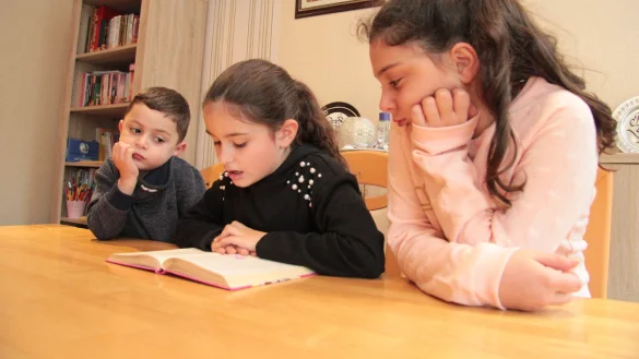 Lesestunde: Die neunj&auml;hrige Ikra (Mitte) liest ihrem kleinen Bruder Salih (5) und ihrer gro&szlig;en Schwester Ela (11) vor. - &copy; Carolin Brokmann-F&ouml;rster