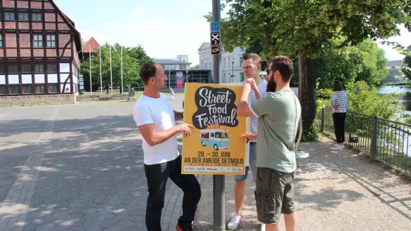 Werben f&uuml;r die Veranstaltung: (von links) Karsten Arning (&bdquo;Stadtlicht" Lemgo), Johannes Strake (&bdquo;Hermanns Club") und Rico Falk (&bdquo;Burrico") h&auml;ngen an der Ameide ein Plakat auf. Kommendes Wochenende findet hier das Street-Food-Festival statt. - &copy; Jana Beckmann