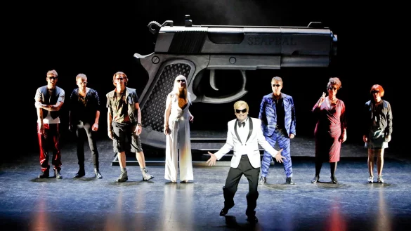 Auf dem Ball: (von links) Benvolio (Hartmut Jonas), Romeo (Lukas Schrenk), Mercutio (Hubertus Brandt), Lady Capulet (Marie Luisa Kerkhoff), Vater Capulet (Holger Teßmann), Tybalt (Stephan Clemens), Julias Amme (Kerstin Klinder) und Julia (Nicola Schubert) feiern ein wildes Fest. Markant ist die Pistole im Hintergrund der Bühne.  - © Landestheater/Birgit Hupfeld