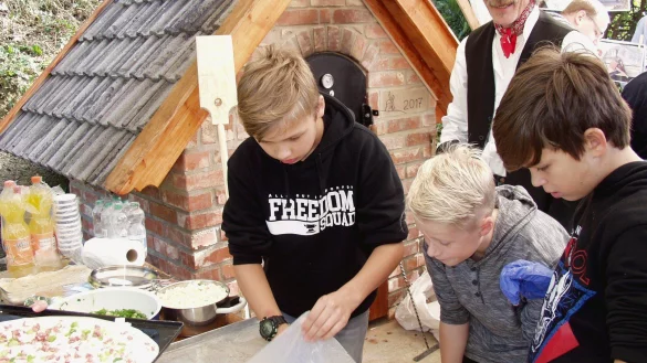 Vorzeigeprojekt: Am neuen Backhaus in Bavenhausen bereiten Jona, Leon und Jamie die Flammkuchenbleche vor (von links). Im Hintergrund Projektleiter Bruno Rischmüller-Affeldt. - © Wulf Daneyko