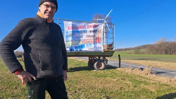 Ulf Allhoff-Cramer vor einem Plakat, das auf die Zerstörung durch den Klimawandel aufmerksam macht. - © Carolin Brokmann-Förster