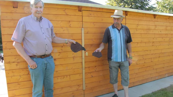 Hartmut Laumeier (links) und J&uuml;rgen Reese haben noch zwei der ausgerissenen Dachschindeln auf der Siekwiese gefunden. Die T&uuml;r der H&uuml;tte hinter ihnen ist notd&uuml;rftig verschraubt, um weitere Diebst&auml;hle zu verhindern. - &copy; Carolin Brokmann-F&ouml;rster