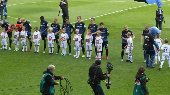 Im Rampenlicht: Die Spieler der JSG SV Diestelbruch-Mosebeck-Kl&uuml;t-Wahmbeck vor den Profis des SCP: (von links) Paderborn-Kapit&auml;n Klaus Gjasula mit Liam Will, Leopold Zingerle mit Joshua Will, Ben Zolinski mit Christoph Meise, Jamilu Collins mit Nick Kraft, Sebastian Vasiliadis mit Lias Weyck, Mohamed Dr&auml;ger mit Liron Maryniok, Luca Kilian mit Josia Brandt, Sebastian Schonlau mit Ben-Kaleb Rahn, Cauly Oliveira Souza mit Tim Budde, Kai Pr&ouml;ger mit Ole Hoffmann, Sven Michel mit Hannes Schmittinger. Das Kind, das mit Maskottchen Holly einl&auml;uft, geh&ouml;rt nicht zur JSG. - &copy; Sebastian Lucas