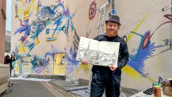 Der K&uuml;nstler Philipp Hiller zeigt sein Skizzenbuch. Die 2015 entstandene H&auml;userzeile von Detmold findet sich auch im Hintergrund auf der Wand wieder. - &copy; Raphael Bartling