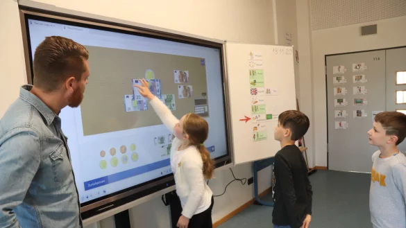 Lara, Mateo und Tyler (von links) schieben Geldscheinbilder auf einen symbolischen Kassentresen. Lehrer Johannes Driediger hat ihnen eine Summe genannt, die sie bezahlen m&uuml;ssen.&nbsp; - &copy; Birgit Guhlke